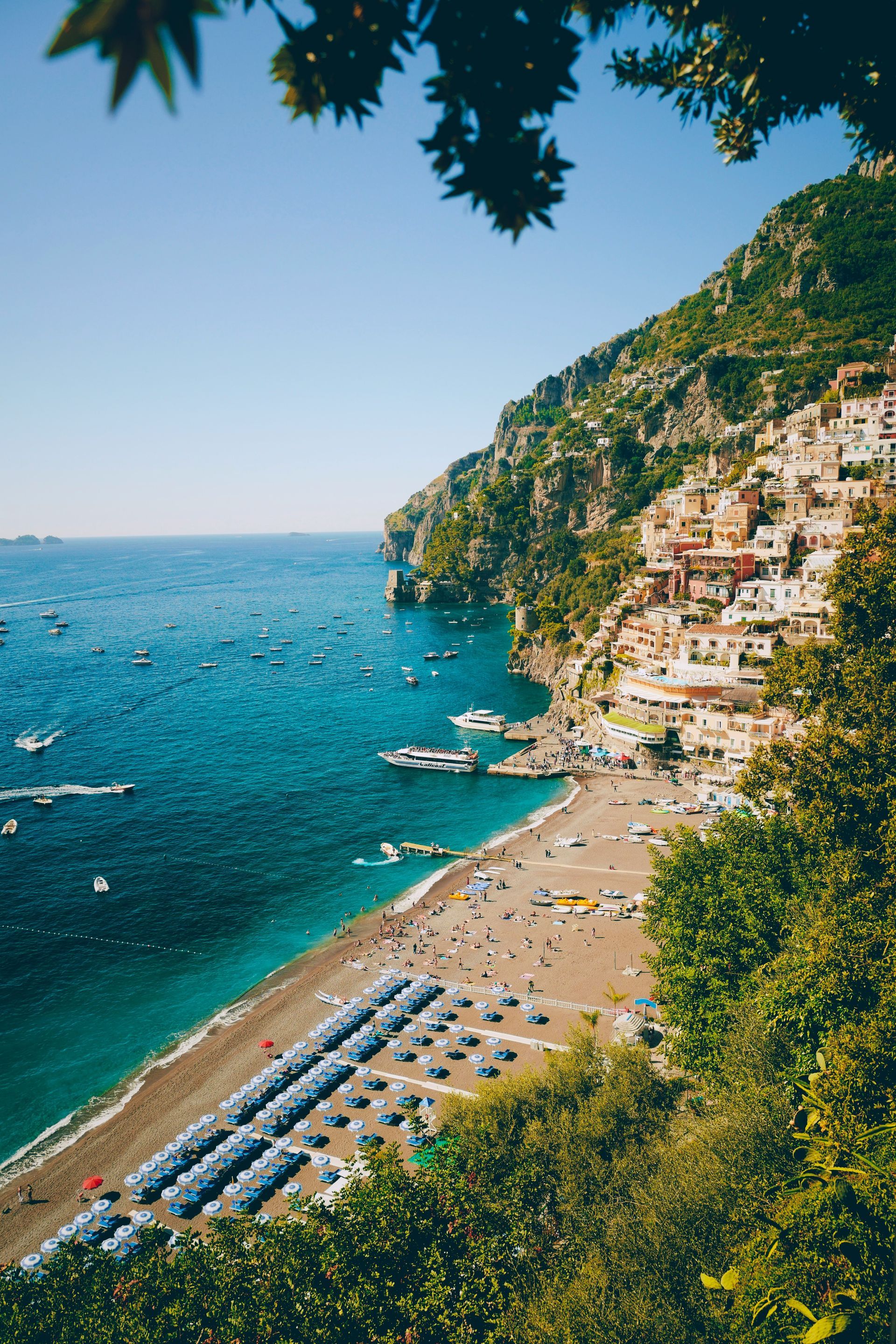 A beach surrounded by mountains and trees next to a body of water on the Amalfi Coast.