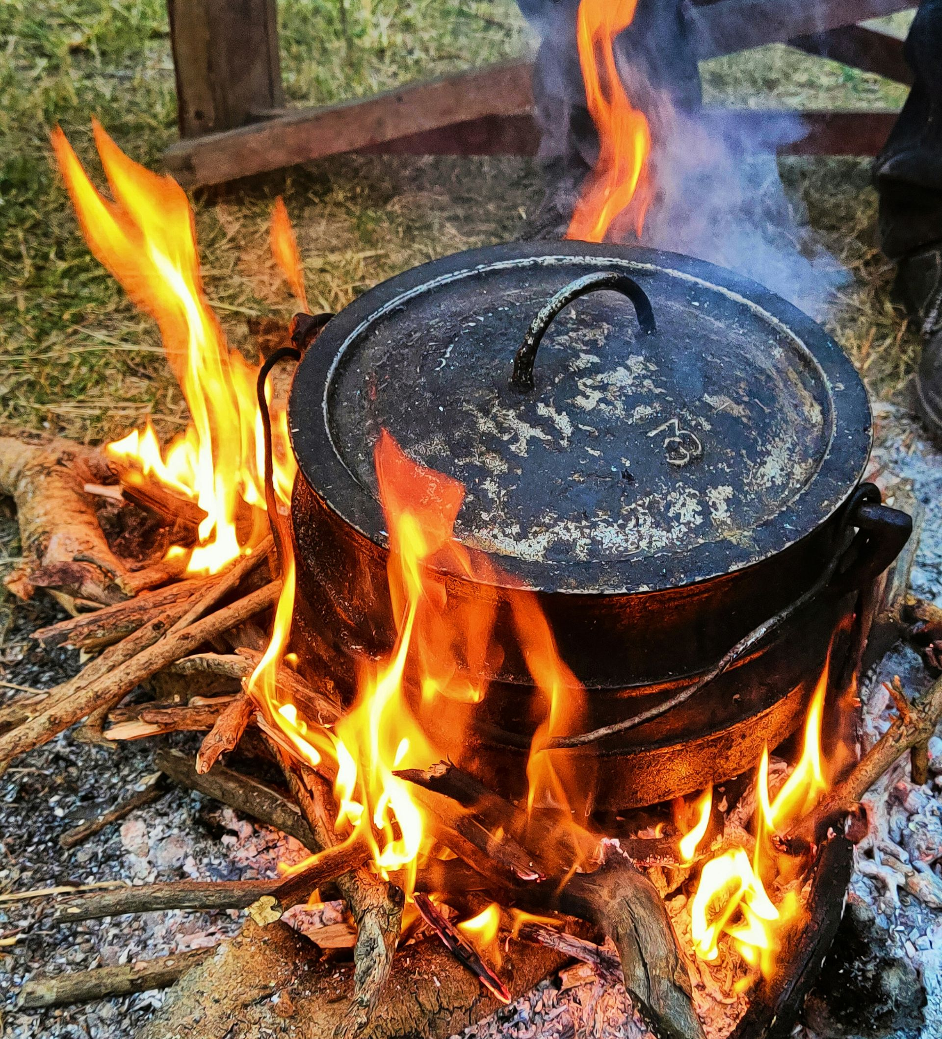 A cast iron pot with lid sits over a roaring outdoor fire, making traditional Potjiekos in South Africa.