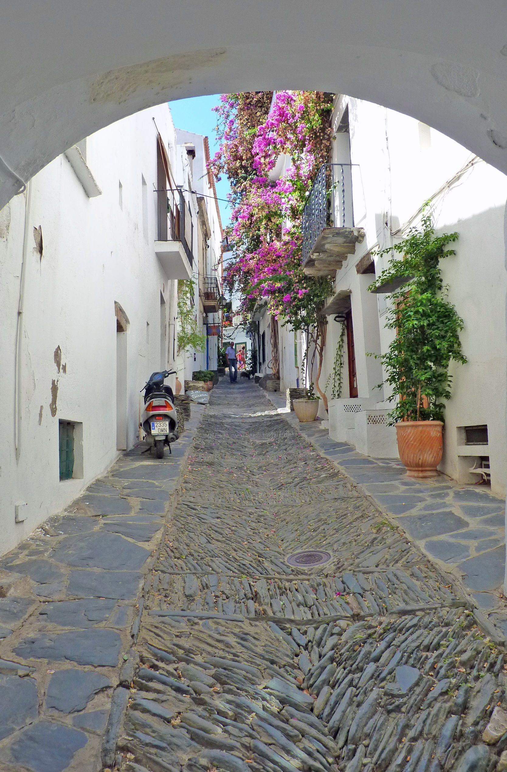A narrow cobblestone street with a motorcycle parked on the side of it in Cadaqués, Spain.