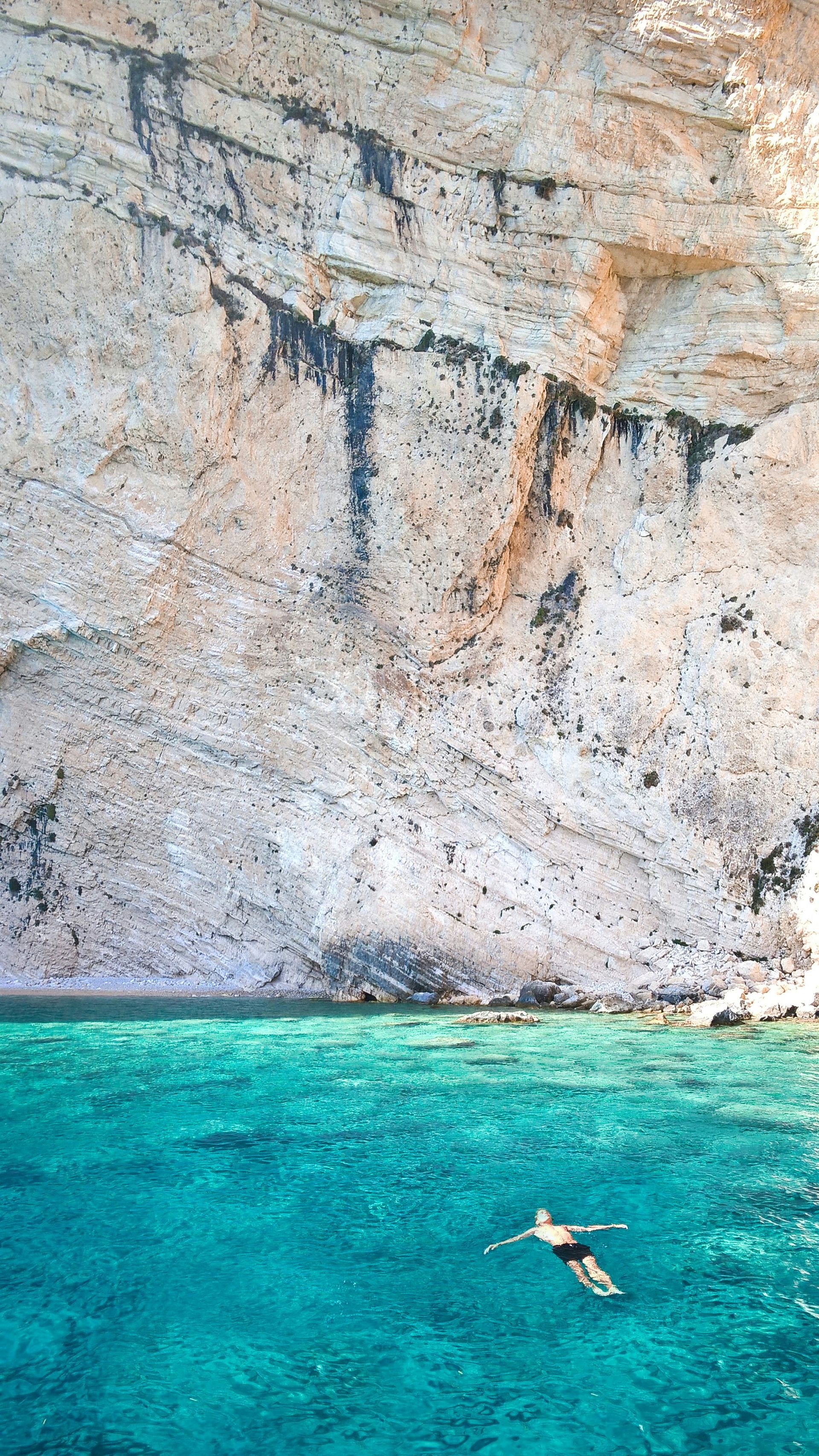 A man is swimming in the ocean near a rocky cliff in Zakynthos, Greece.