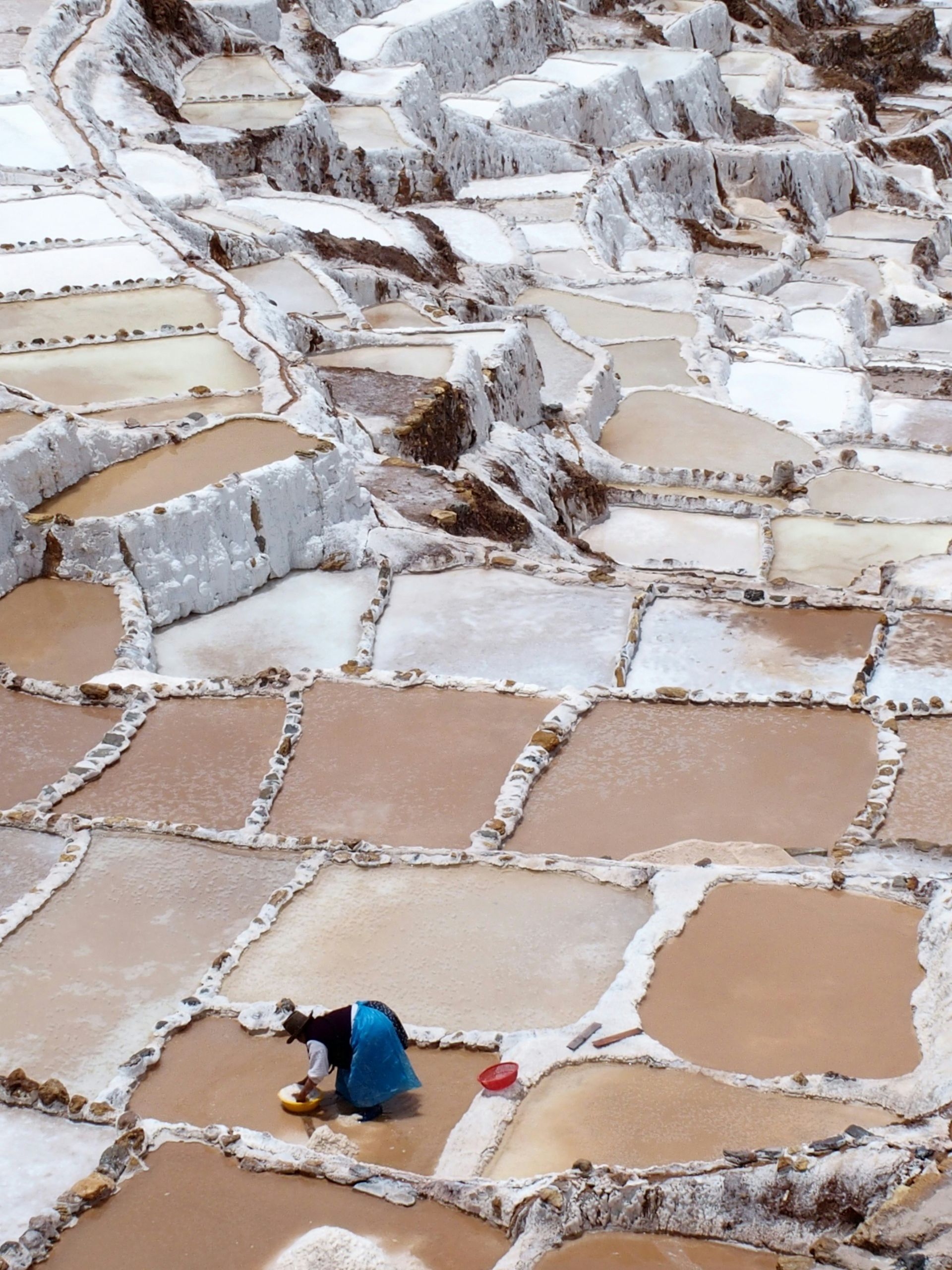 A woman is kneeling down in the Maras Salt Mines in Peru.