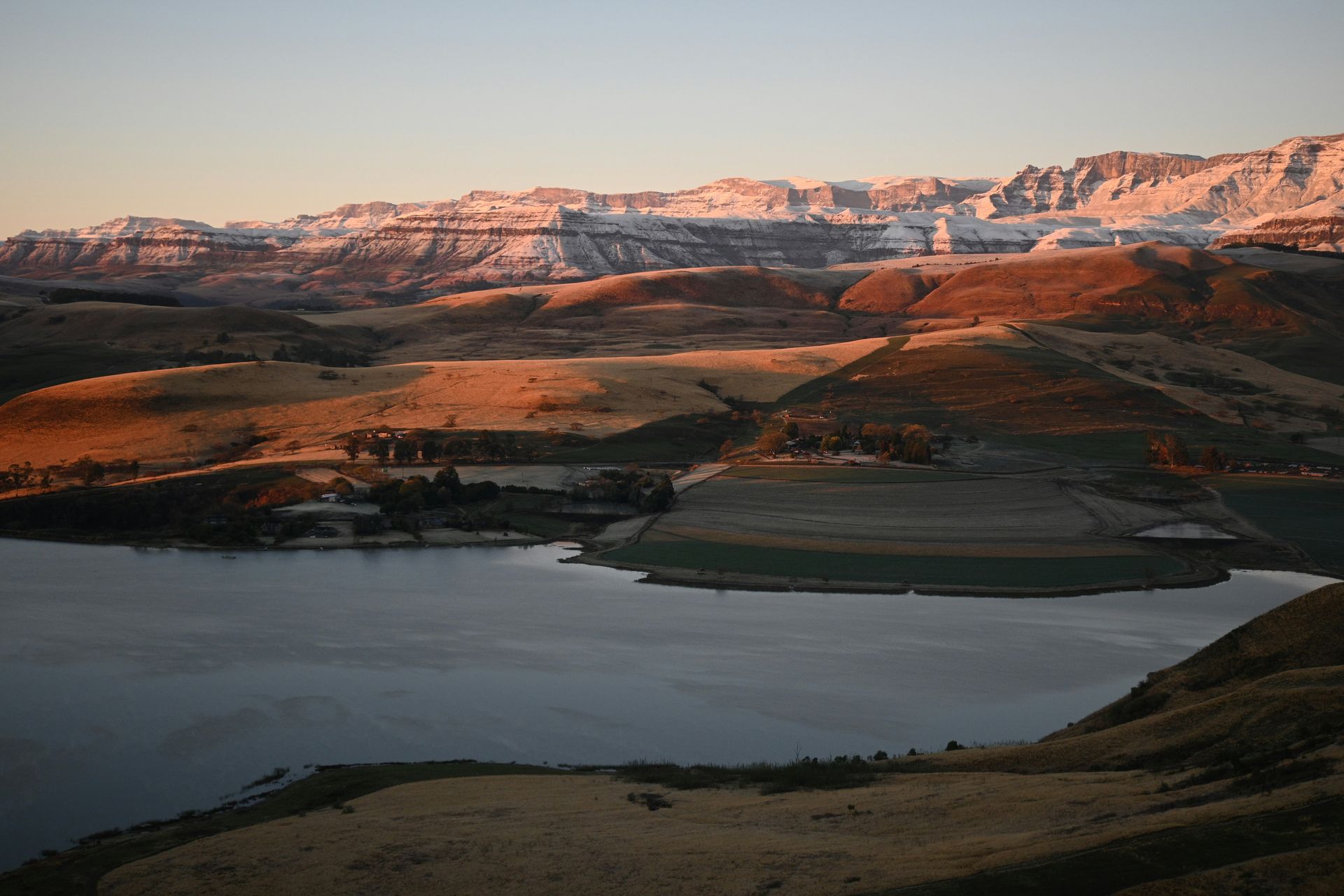 Lake and rolling hills at sunset, mountains in background with snow, in the Drakensberg, South Africa.
