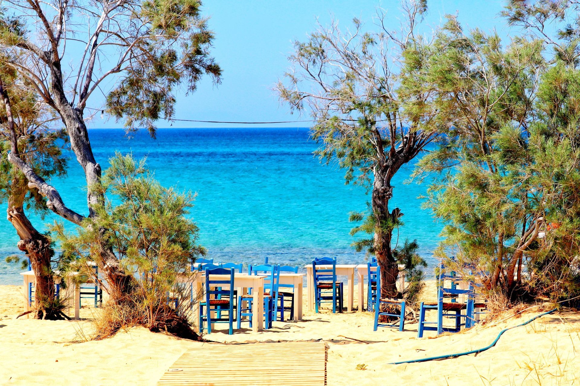 A beach with blue chairs and umbrellas in front of the ocean in Naxos, Greece.