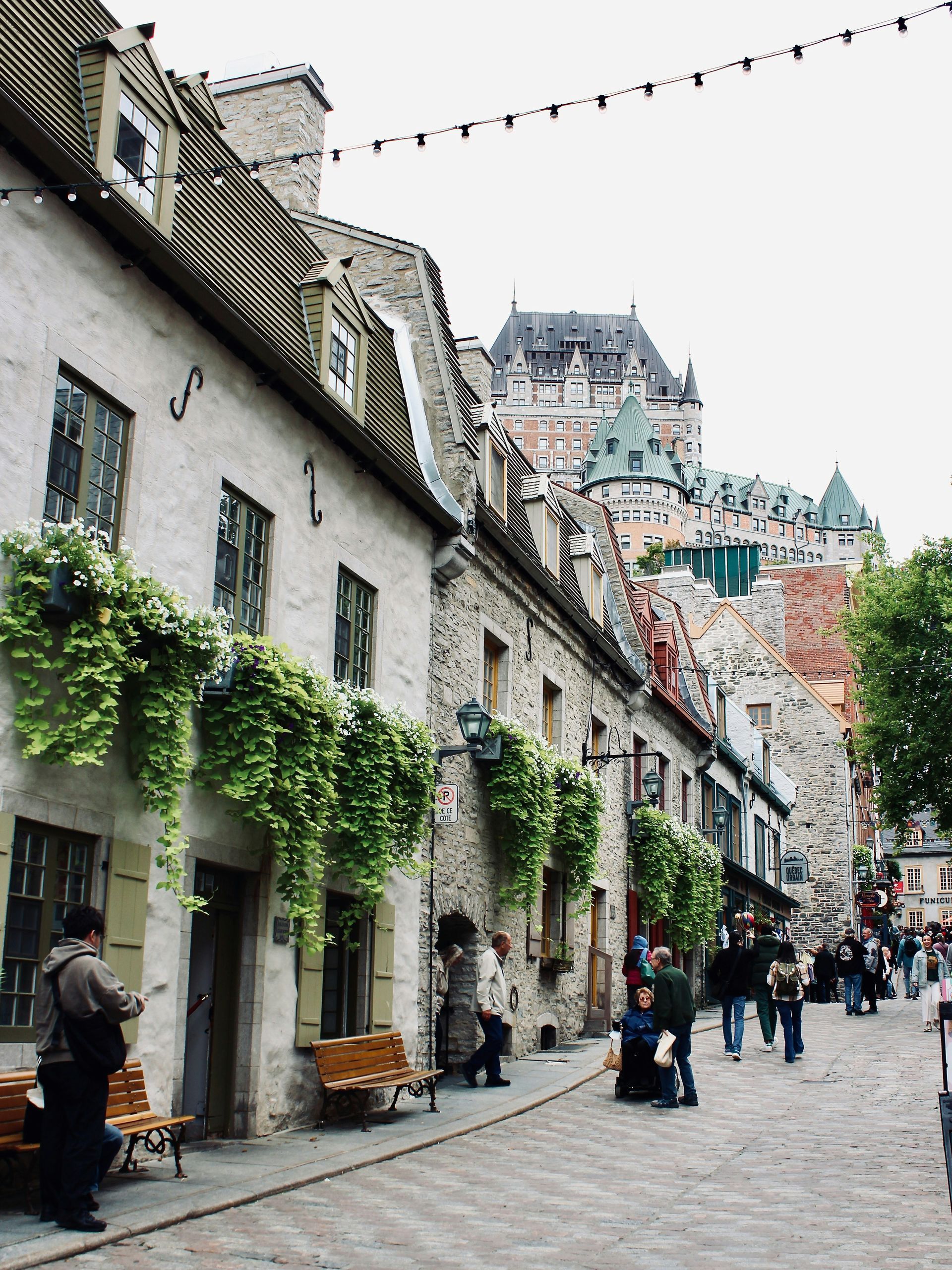 Cobblestone street in Quebec City lined with historic buildings with Château Frontenac visible in the background.