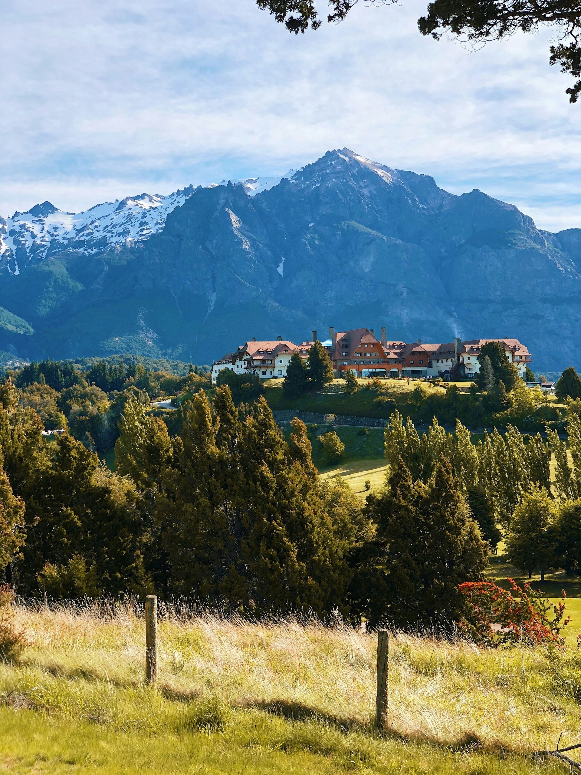 A mountain with snow-capped peaks overlooks a lodge surrounded by trees in San Carlos de Bariloche, Argentina.