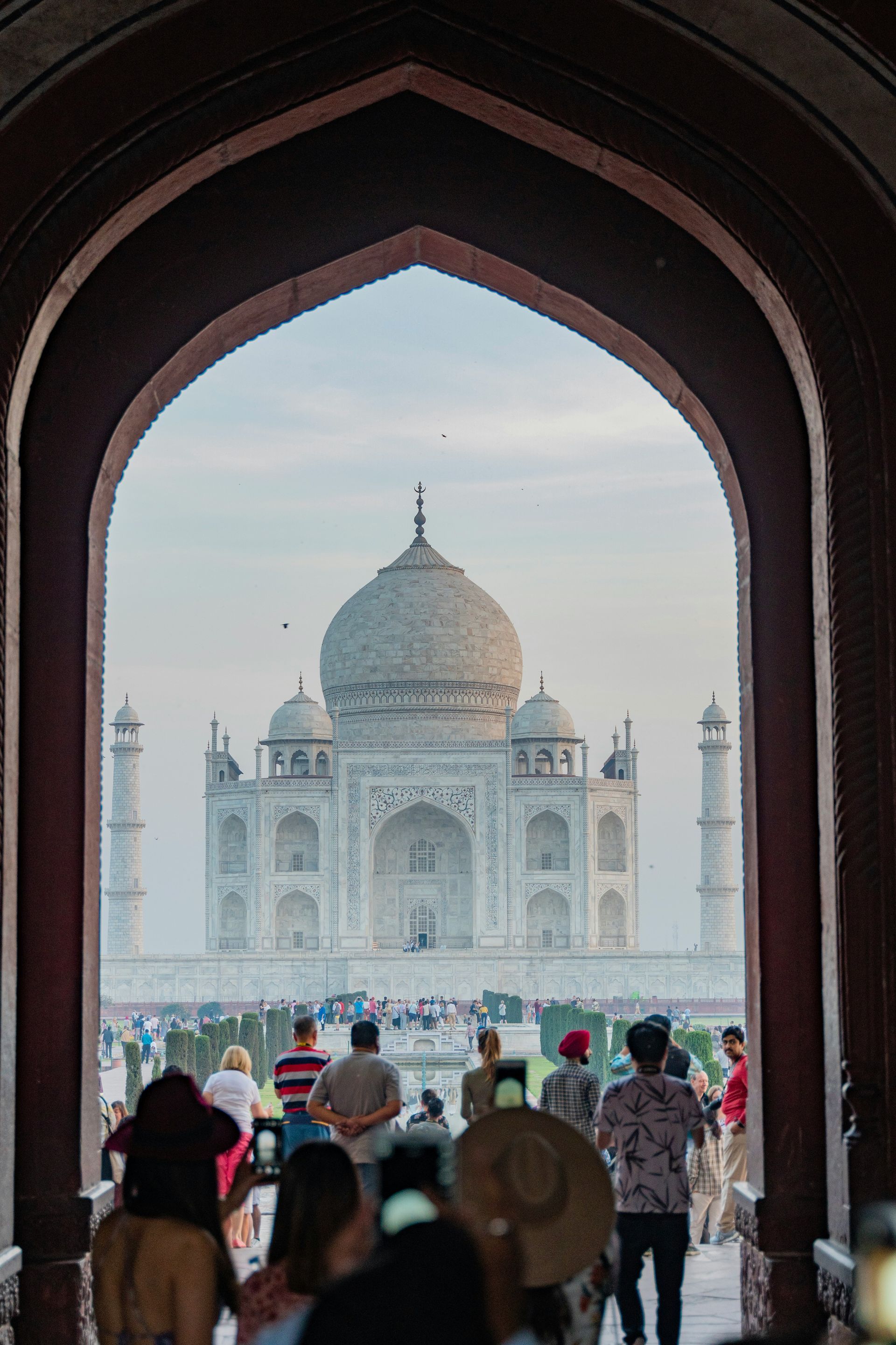 Taj Mahal seen through an arched gateway; tourists stand below in Agra, India.