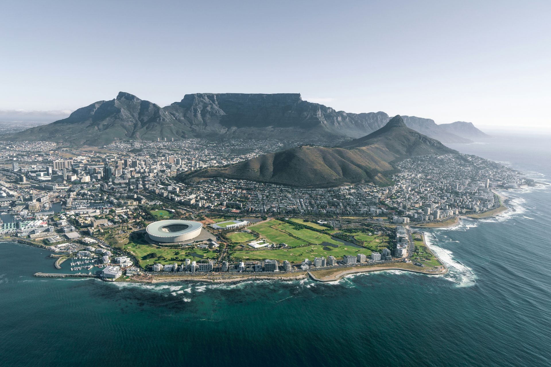 Cape Town, South Africa, aerial view with Table Mountain in the background, stadium, coastline, and city.