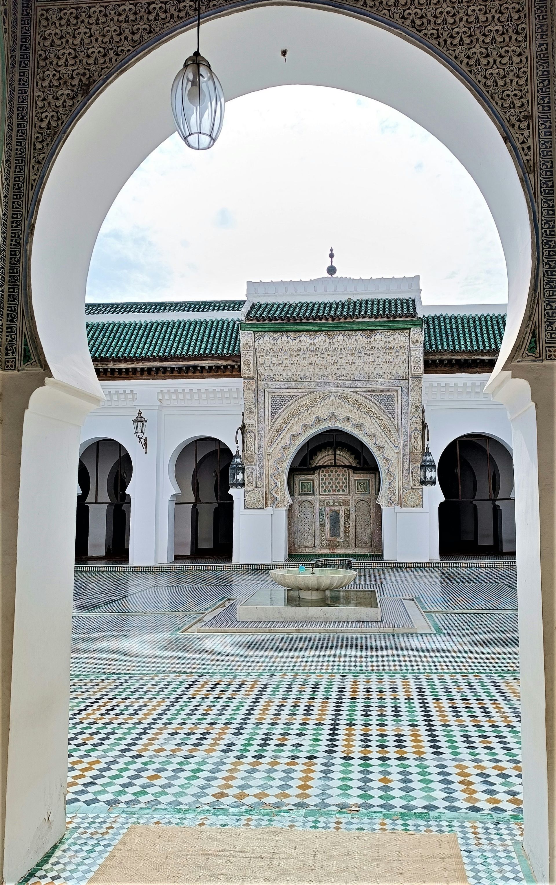 A view of a mosque through an archway with a lantern hanging from the ceiling in Fes, Morocco.