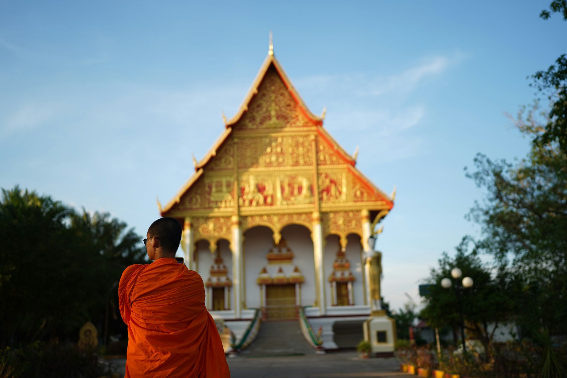 Buddhist monk in orange robes facing a golden temple in Vientiane, Laos.