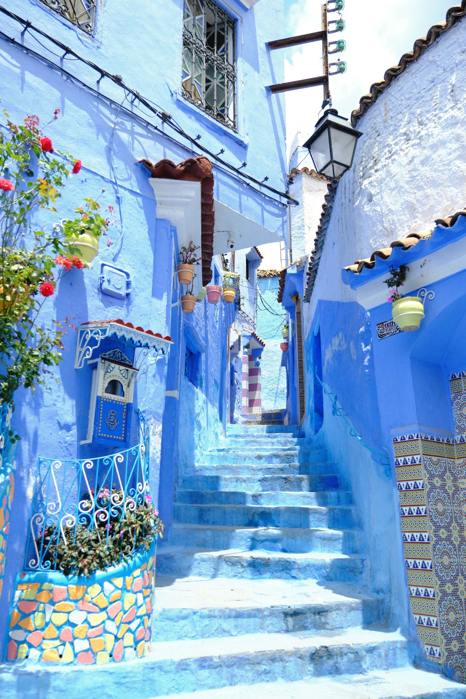 A narrow alleyway with stairs leading up to a blue building in Chefchaouen, Morocco.