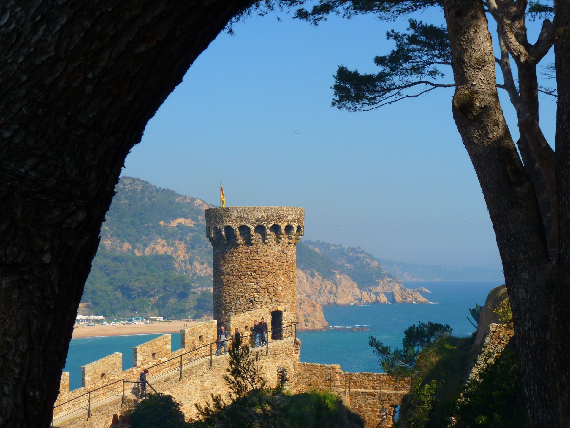 A stone tower is surrounded by trees overlooking the ocean in Tossa de Mar, Spain.
