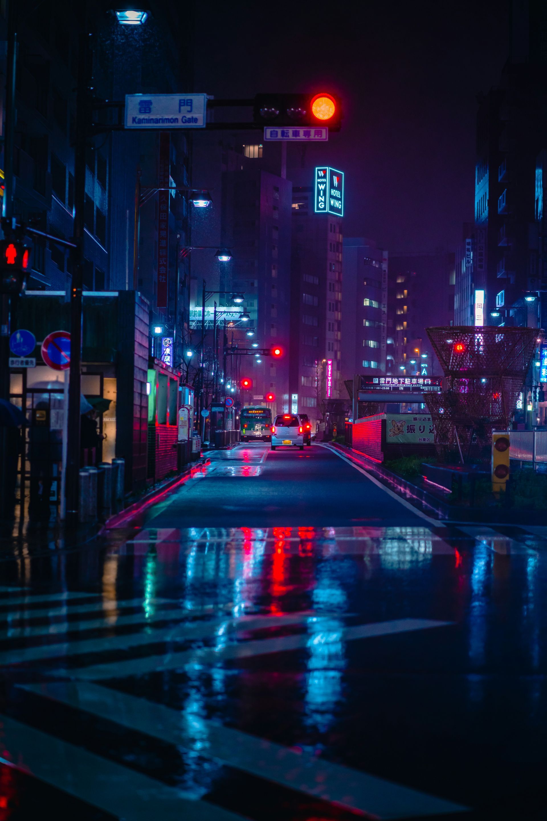 Neon-lit street in Tokyo, Japan reflecting lights on wet pavement. Red traffic lights glow amidst the blue hues.