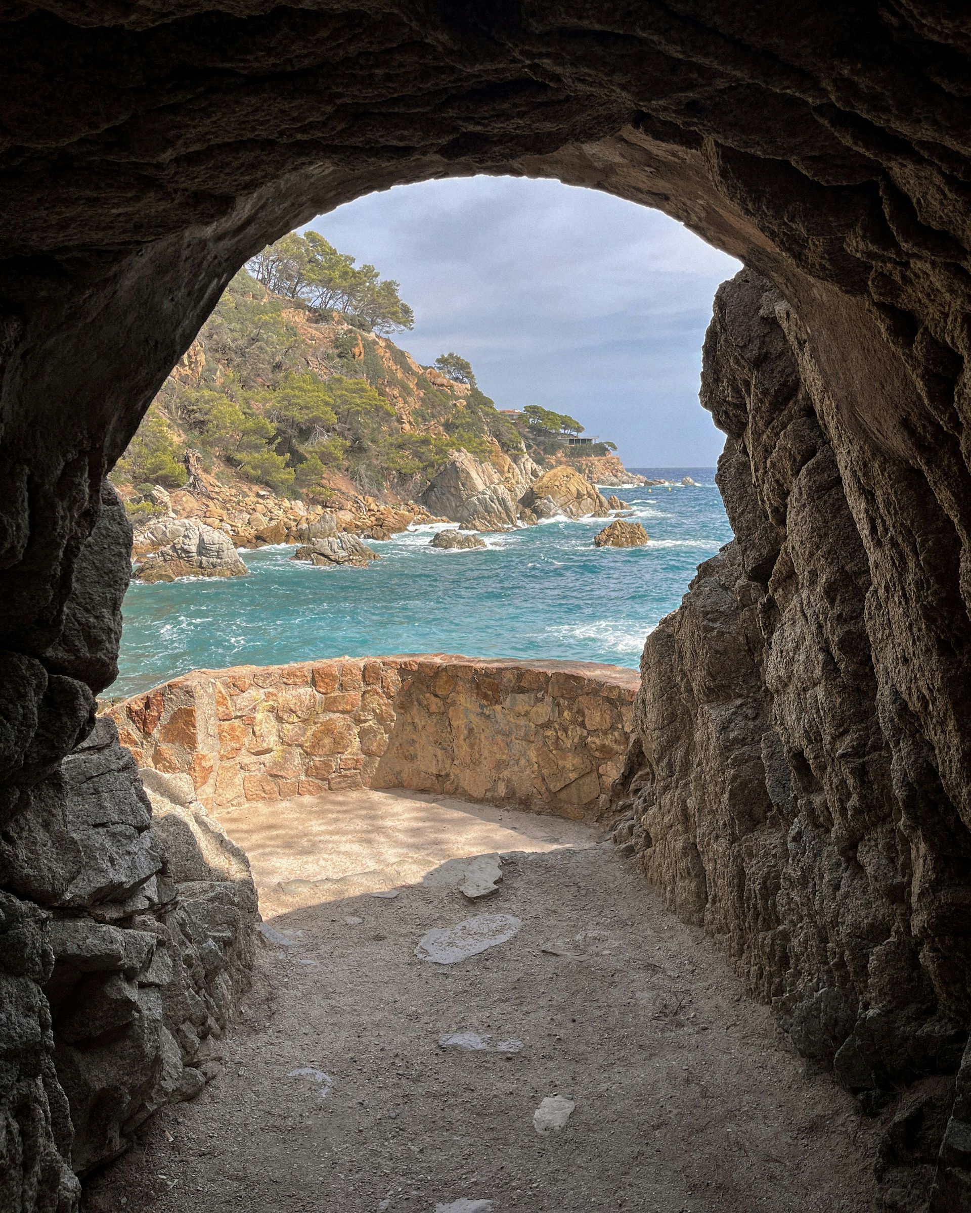 Tunnel opening to a coastal view: turquoise water, rocky cliffs, and blue sky on Costa Brava, Spain.