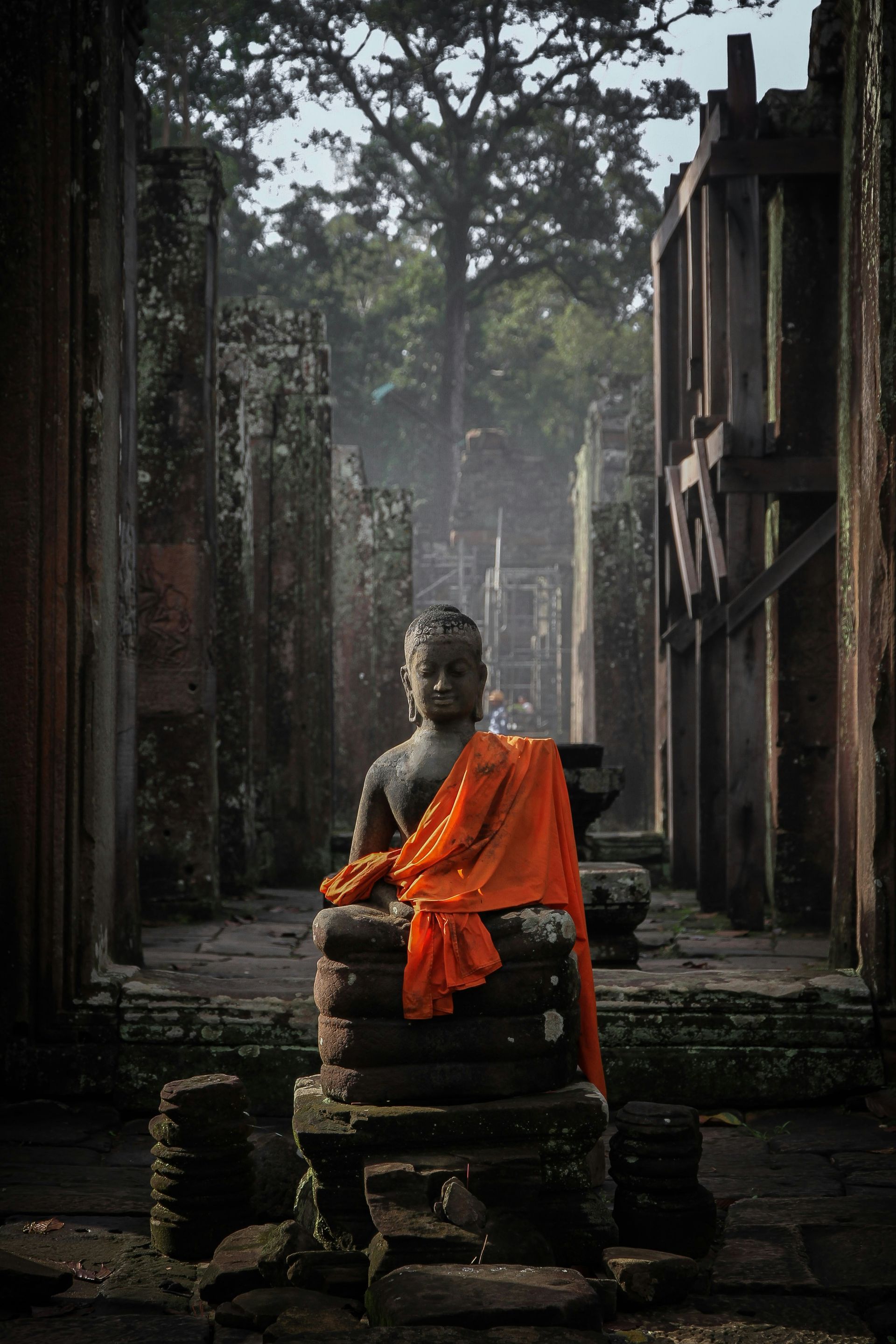 Buddha statue draped in orange cloth, seated in ancient, weathered temple in Siem Reap, Cambodia.