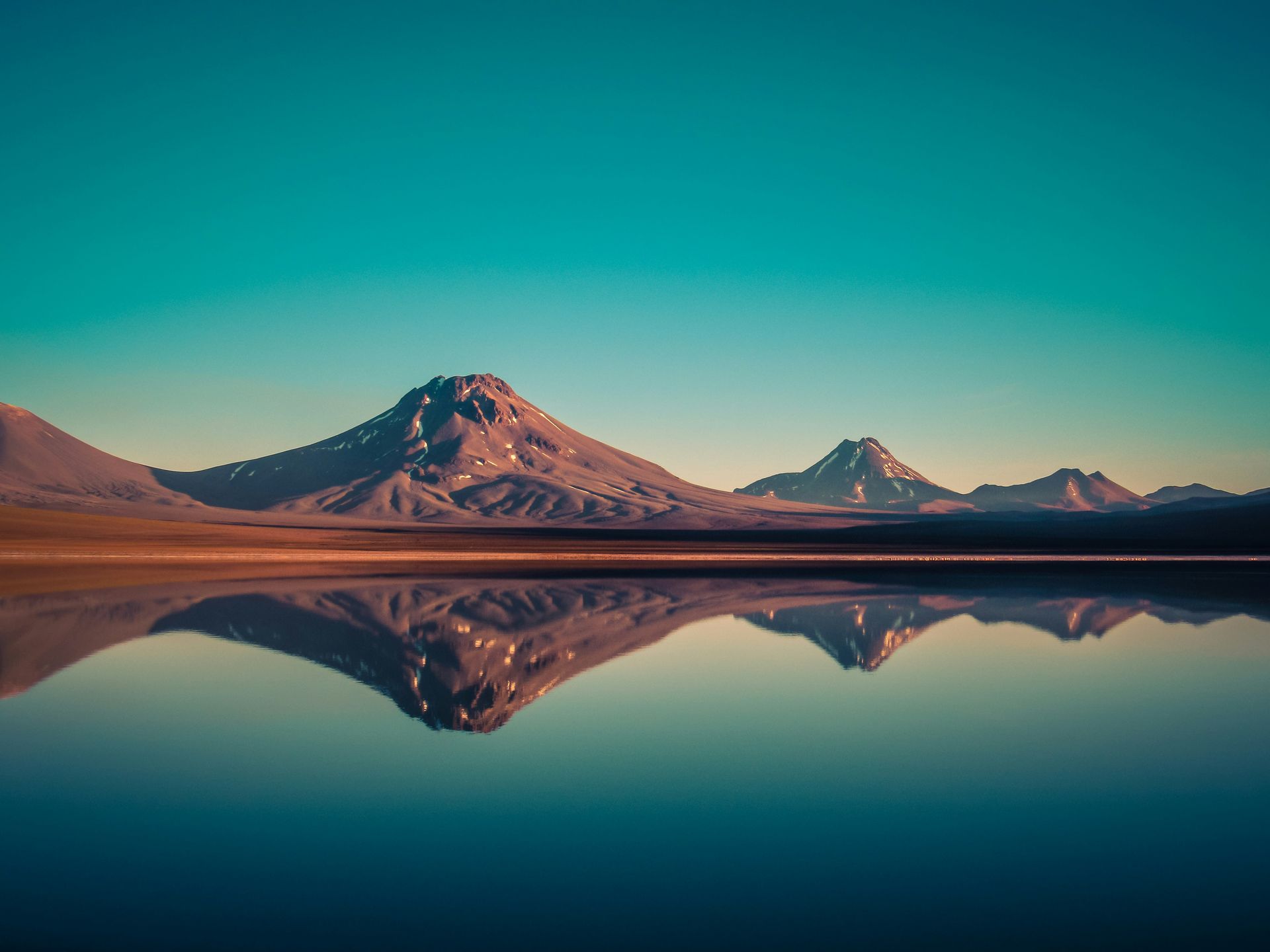 Mountains reflected in the Laguna Lejia lake under a turquoise sky in the Atacama Desert, Chile.