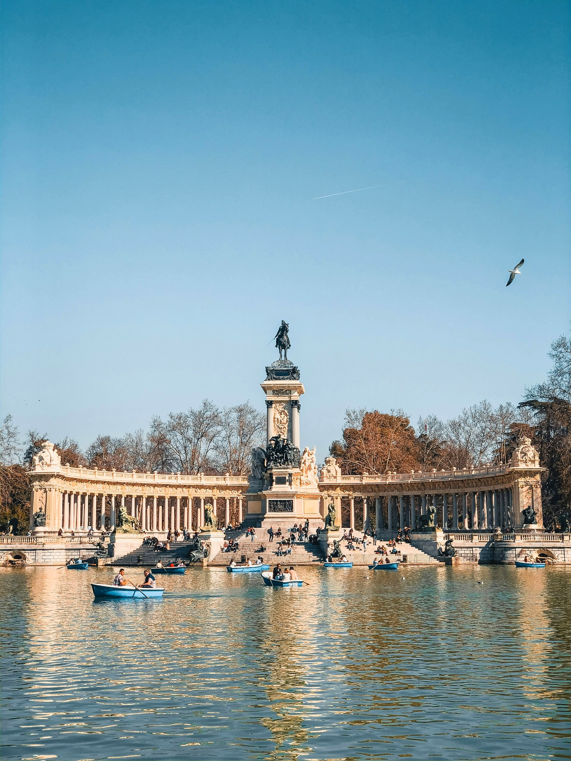 A park scene with a large monument, a lake with rowboats, and a clear blue sky in Madrid, Spain.