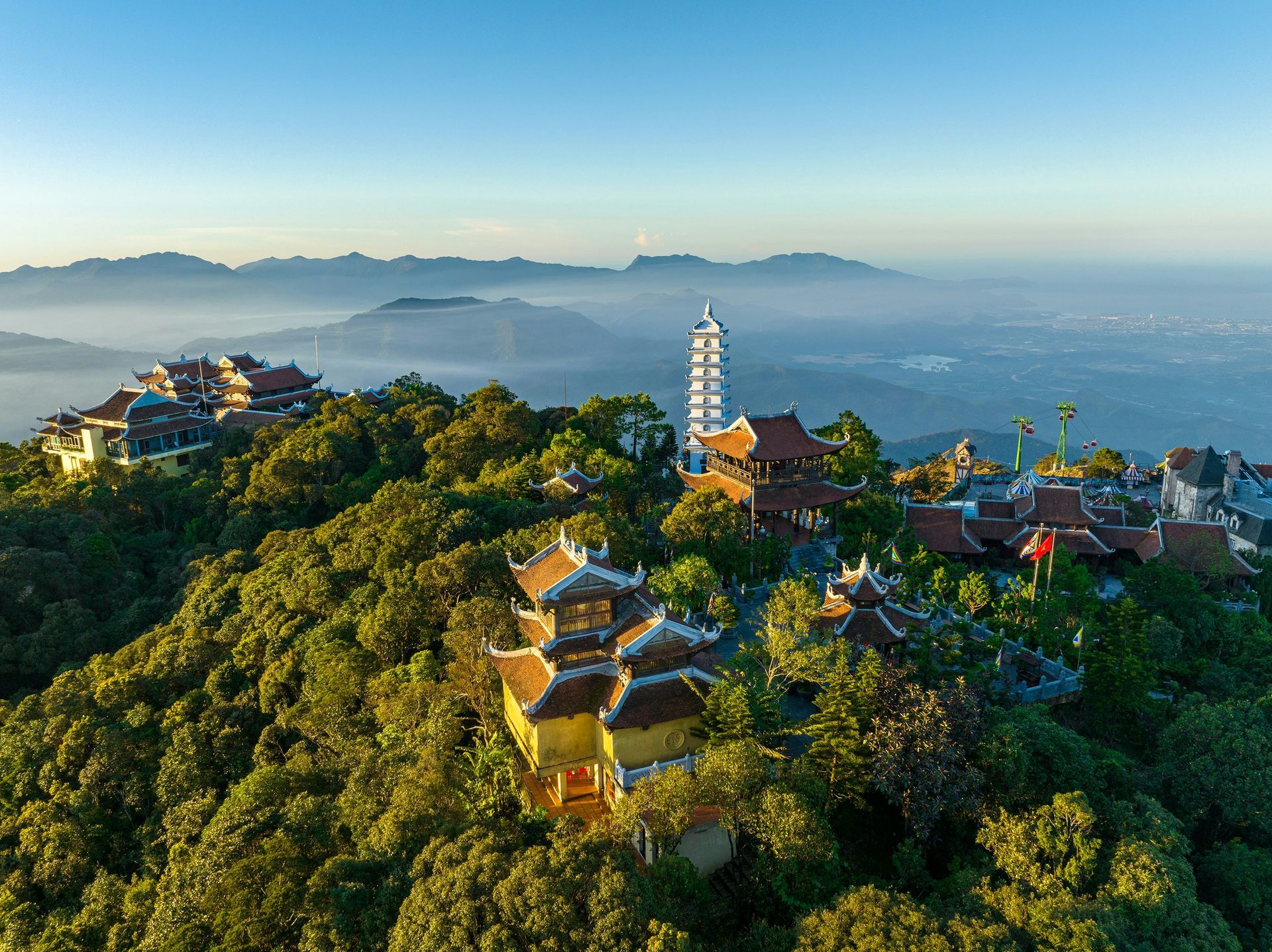 Buddhist temple complex atop a lush green mountain, with a tall white pagoda and misty mountains, in Da Nang, Vietnam.