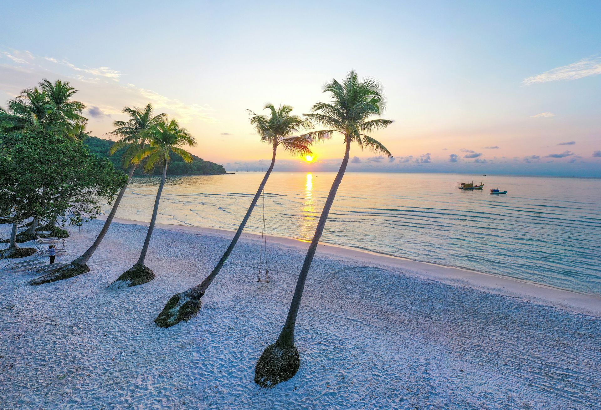 Palm trees lean over a white sand beach at sunset in Phú Quốc, Vietnam.