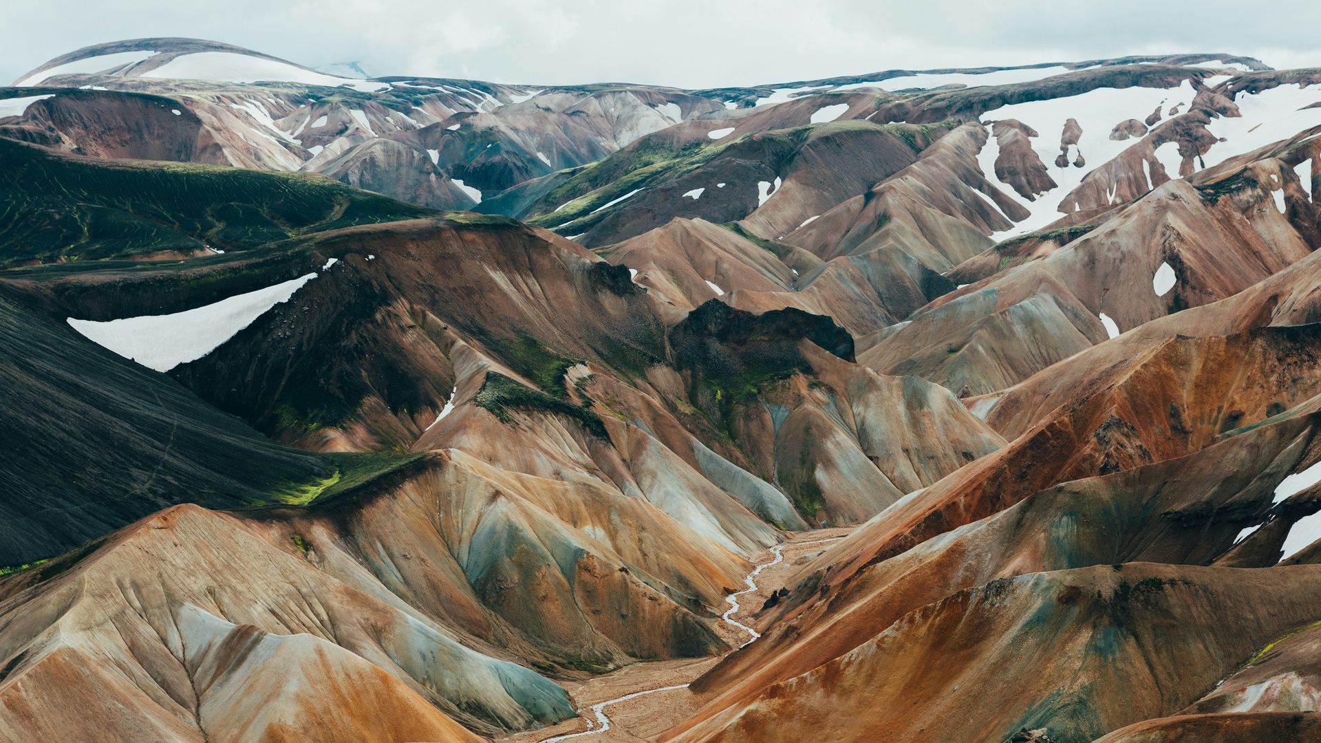 Colorful, layered mountains with patches of snow in a valley landscape in Landmannalaugar, Iceland.