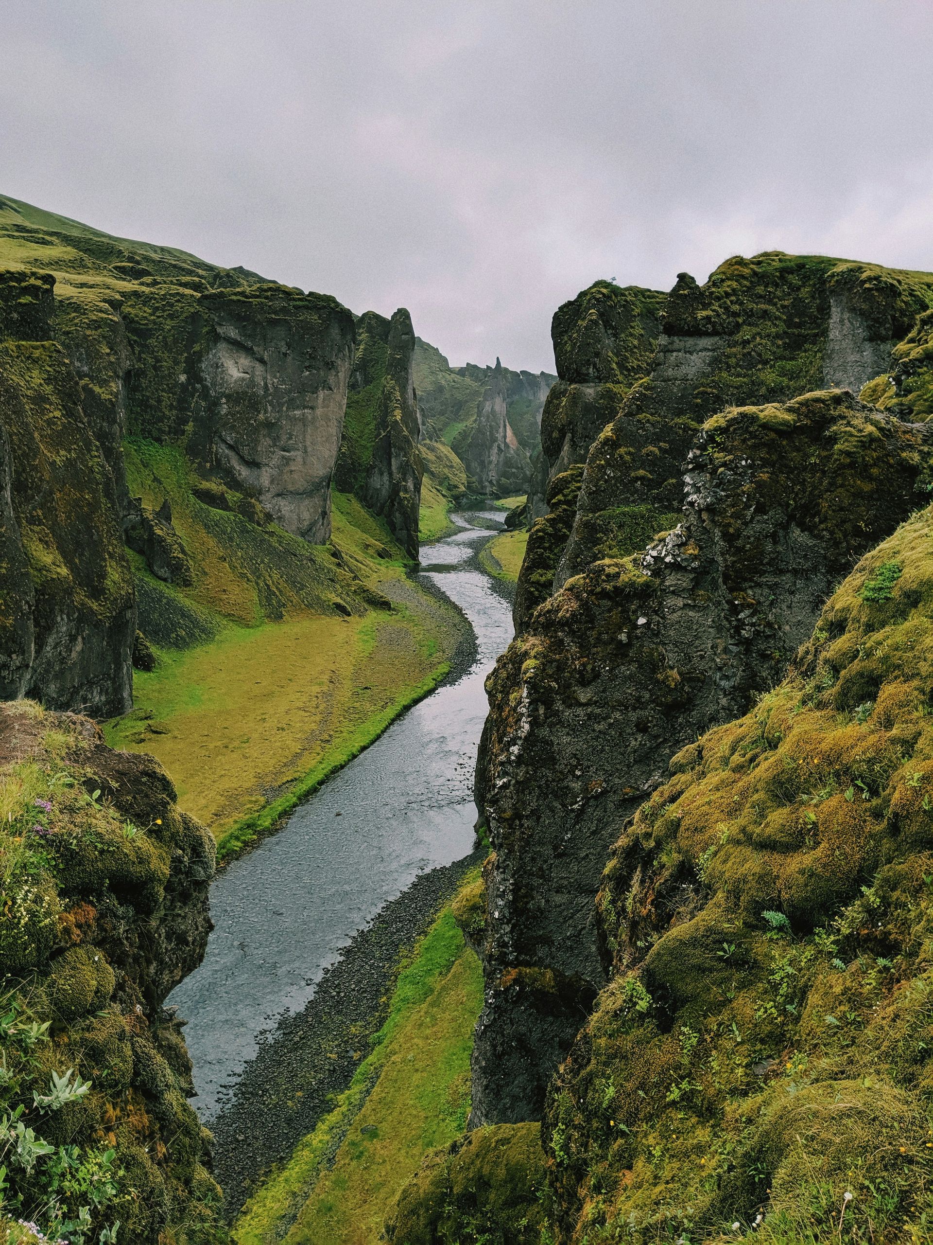 Canyon with a river winding through, green moss and grass on the steep rock walls at Fjaðrárgljúfur Iceland.