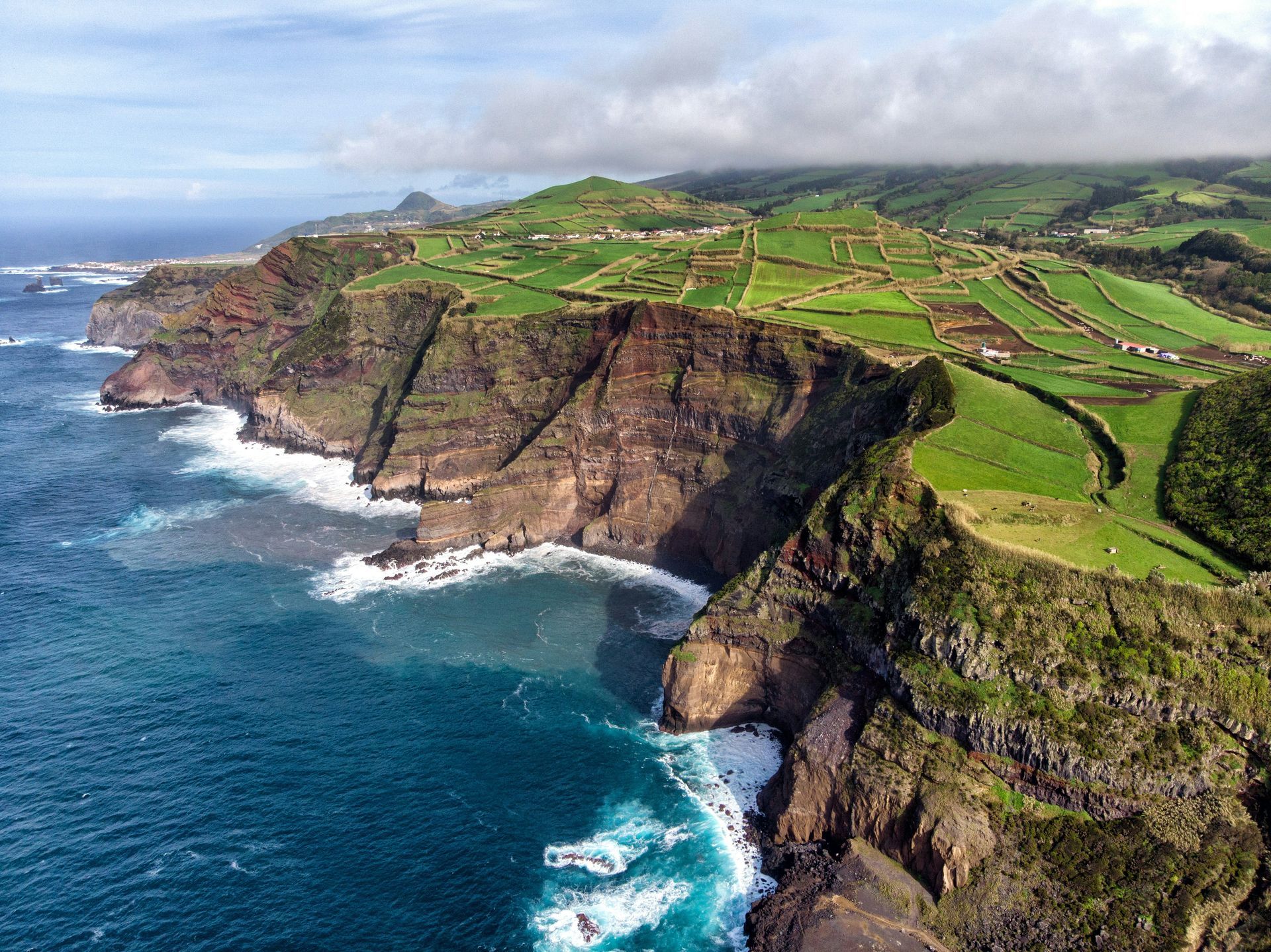 Rugged cliffs meet the deep blue ocean; lush green fields on top, on the island of Azores, Portugal.