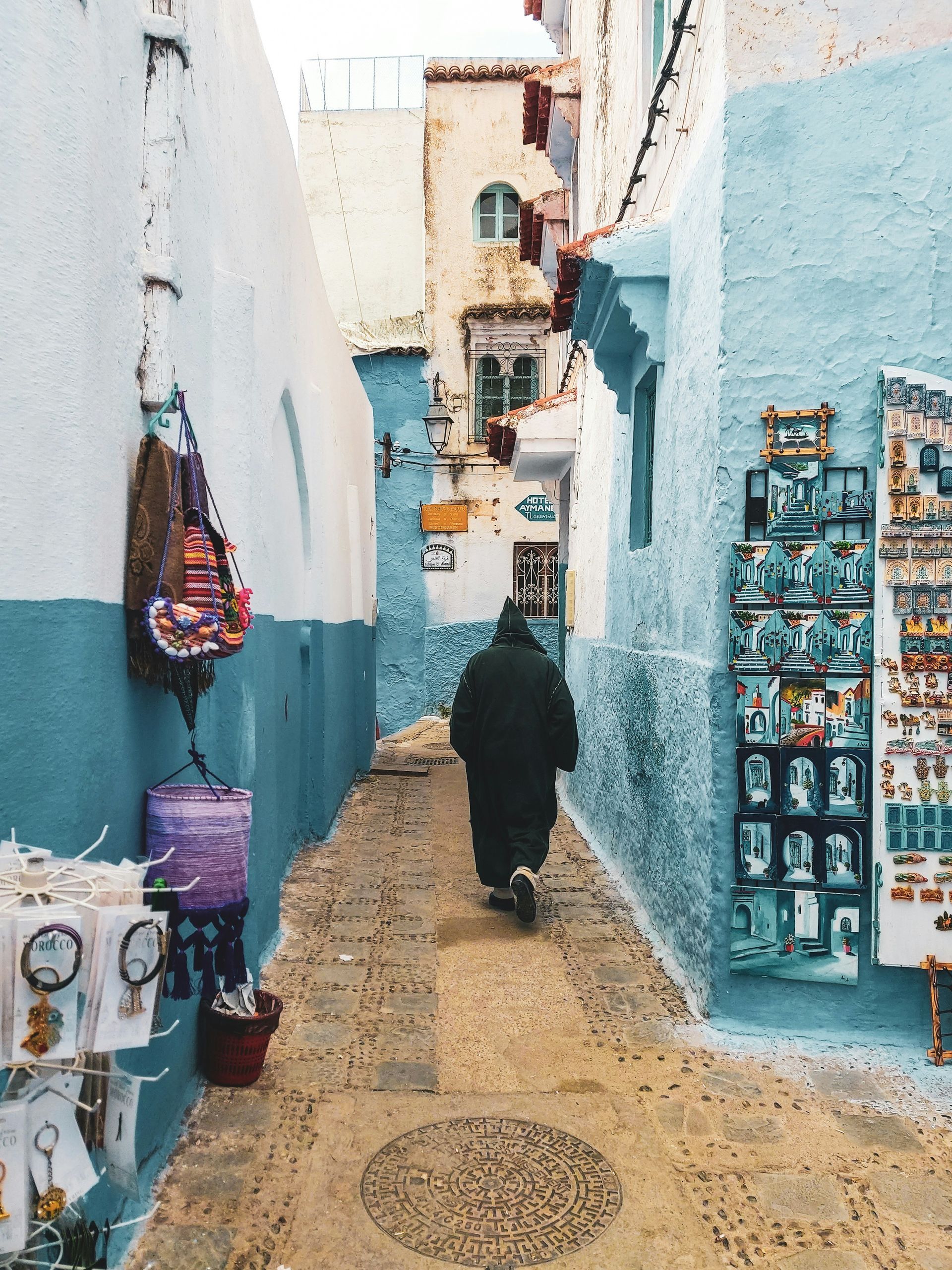A woman is walking down a narrow alleyway between two buildings in Chefchaouen, Morocco.
