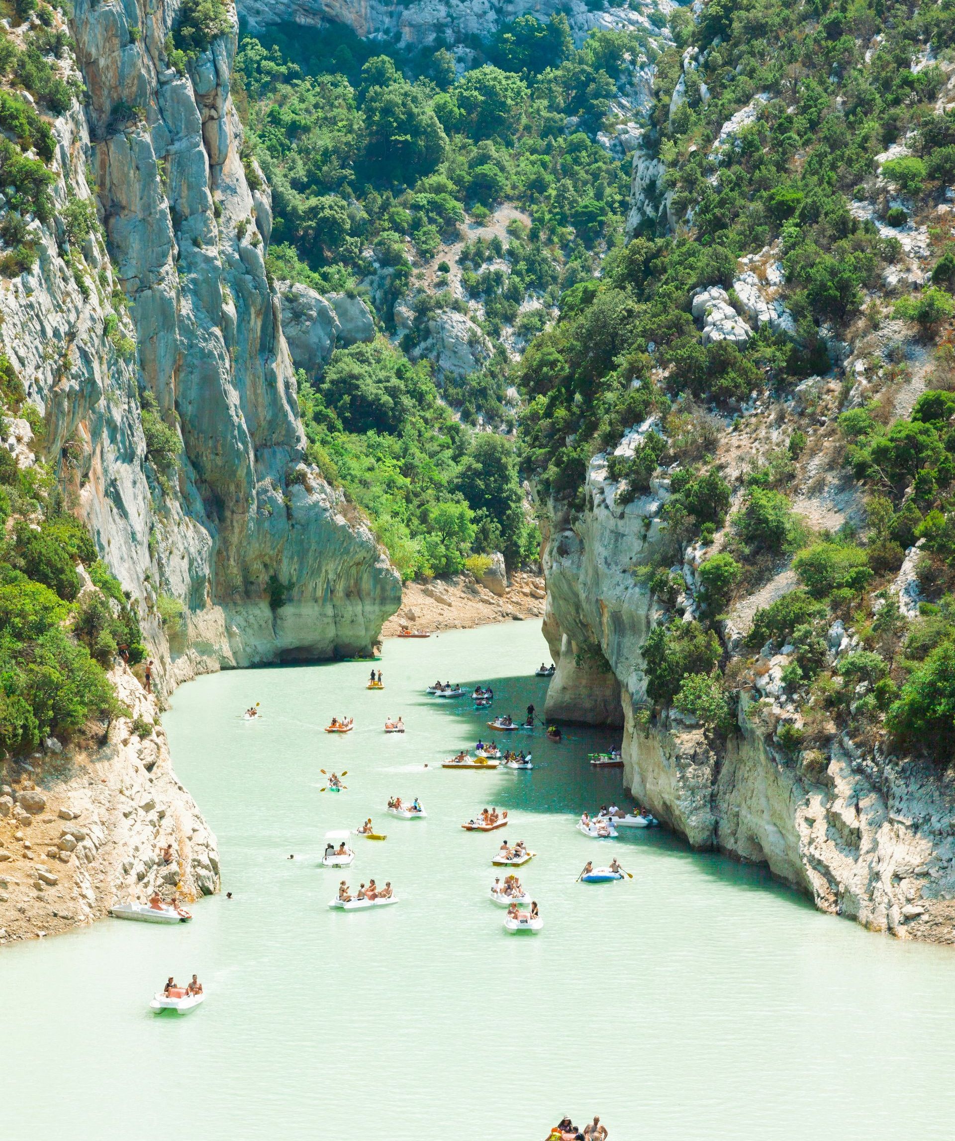 A group of people are floating down the Verdon Gorge surrounded by mountains in France.