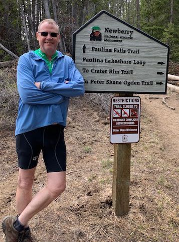 A man is standing in front of a sign in the woods.
