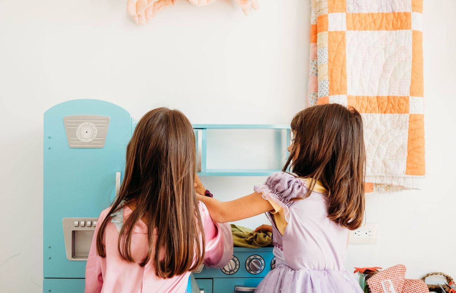 Two little girls are playing in a toy kitchen.