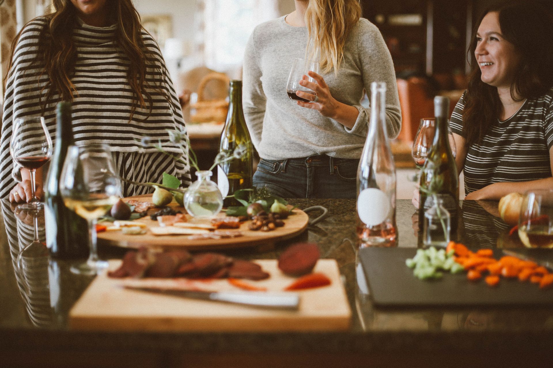 A group of women are standing around a table with food and drinks.