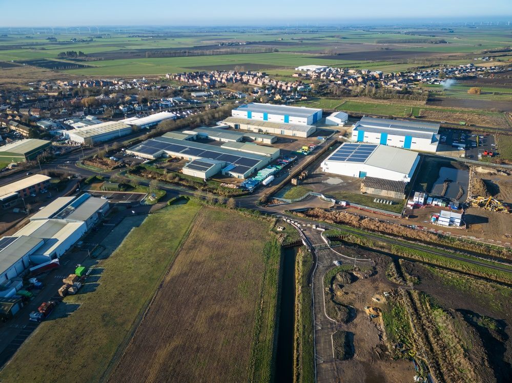 Aerial view of a sprawling industrial park with warehouses and solar panels, adjacent to a residential town and fields.