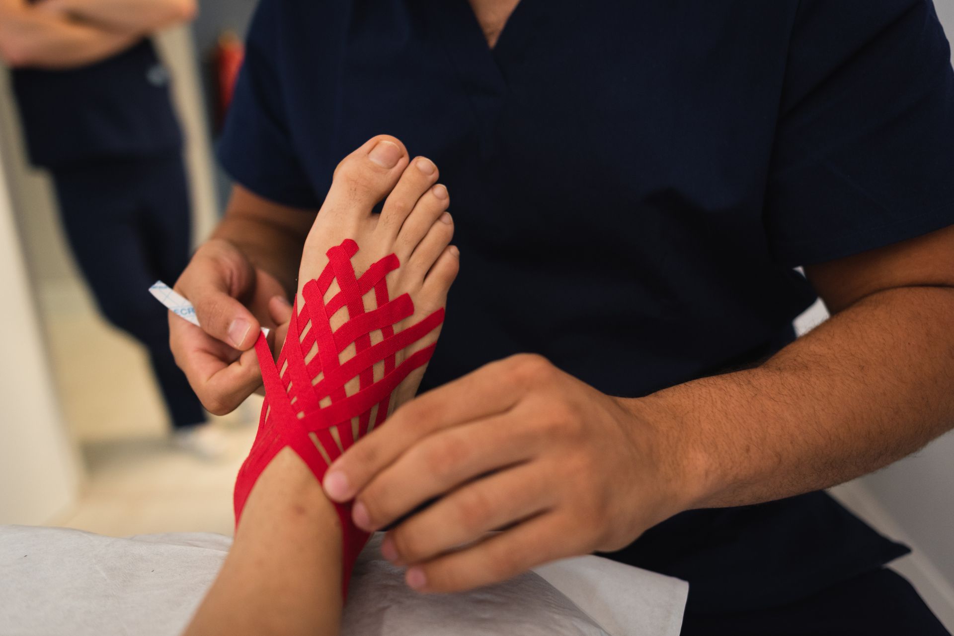 A sports podiatrist applies kinesiology tape to a patient's foot for injury treatment.