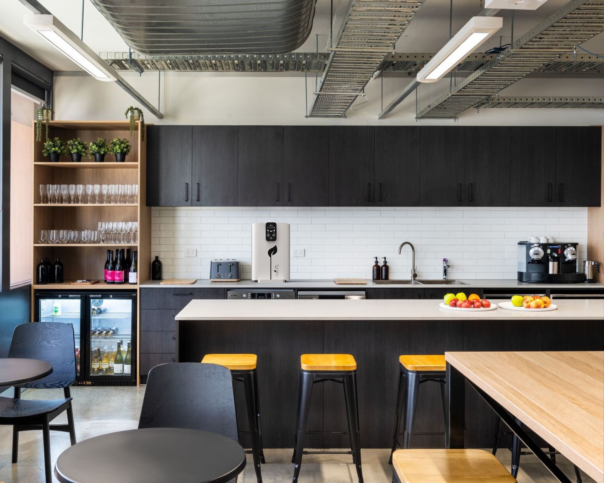 Modern office kitchen with black cabinets, white countertop, bar stools, and a small dining area.