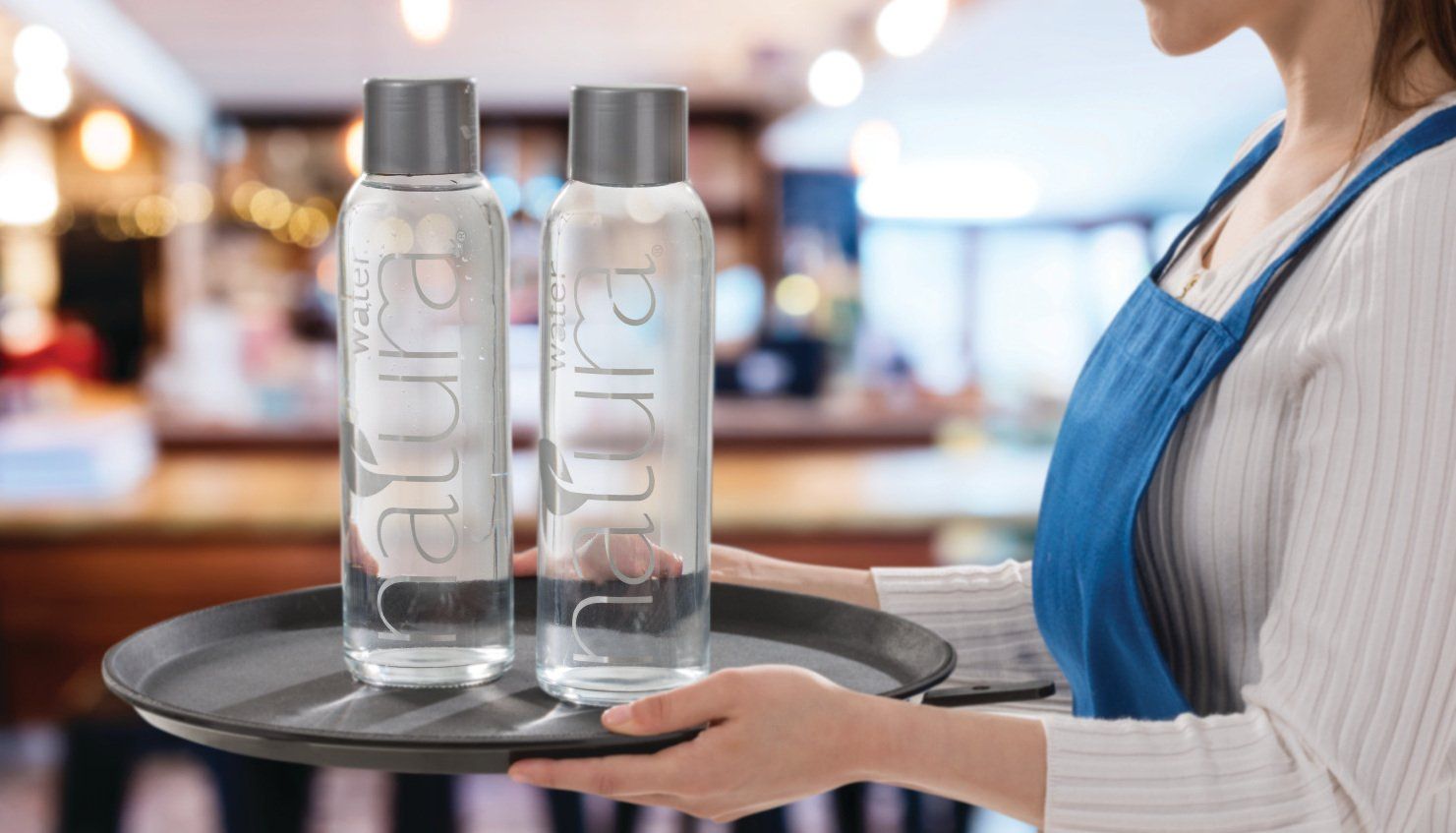 Woman carrying tray with two water bottles labeled