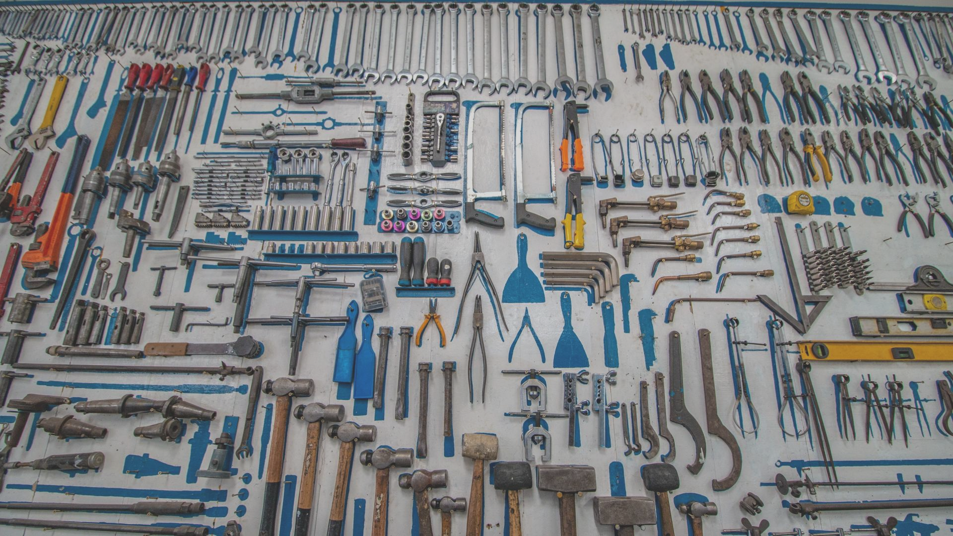 Tools organized on a pegboard, including wrenches, hammers, pliers, and levels, with blue and white accents.