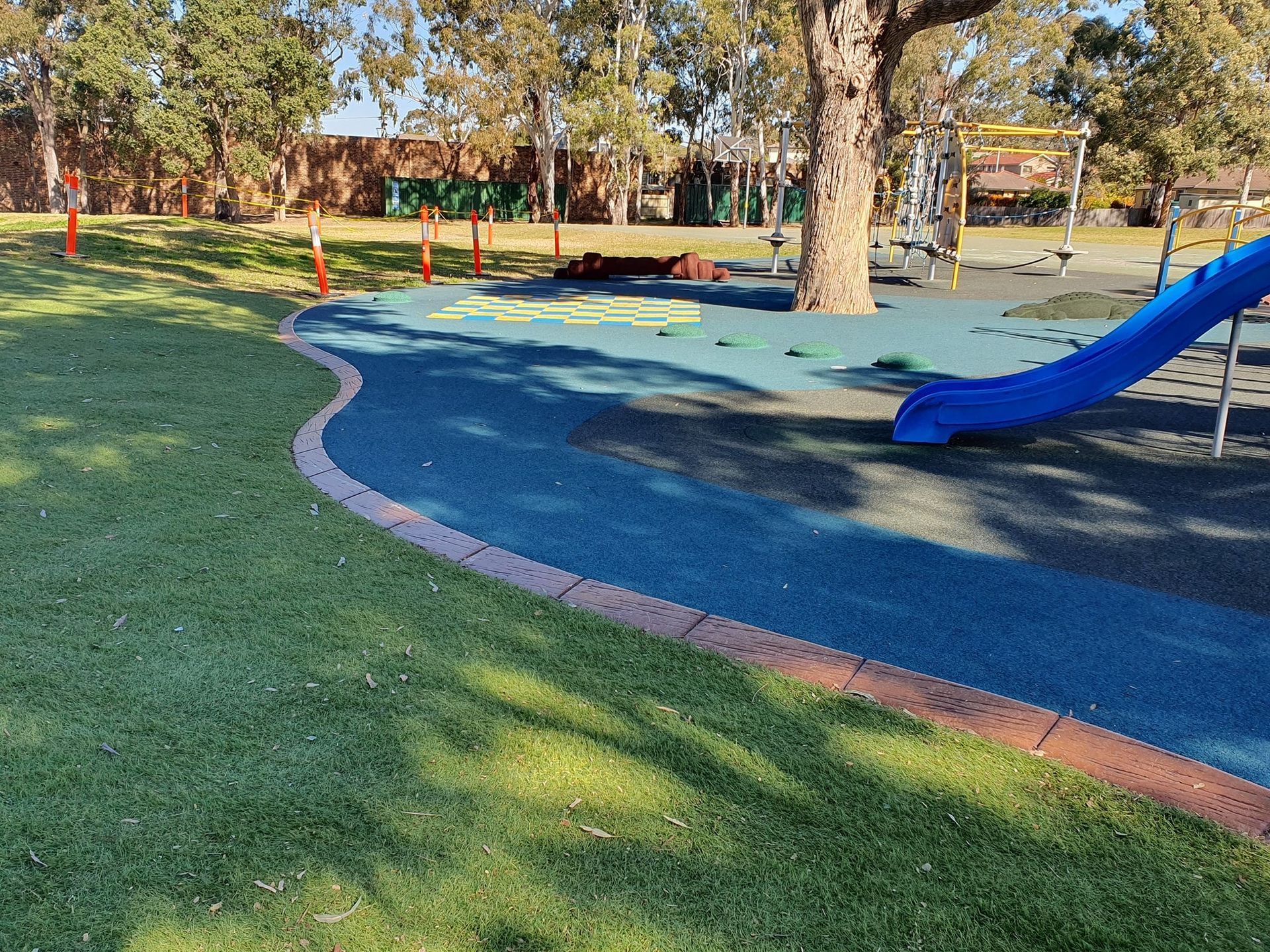 A blue slide in a park with a tree in the background.