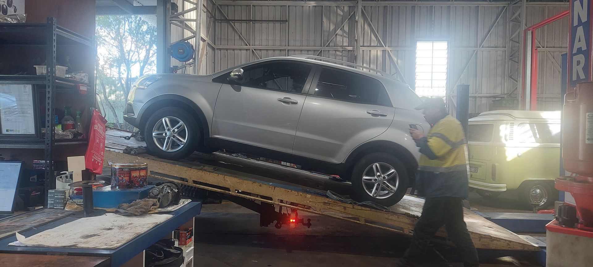 Silver SUV on a tilted tow truck ramp in a garage, with a worker nearby - Bay City Quality Mobile Mechanic In Pialba, QLD