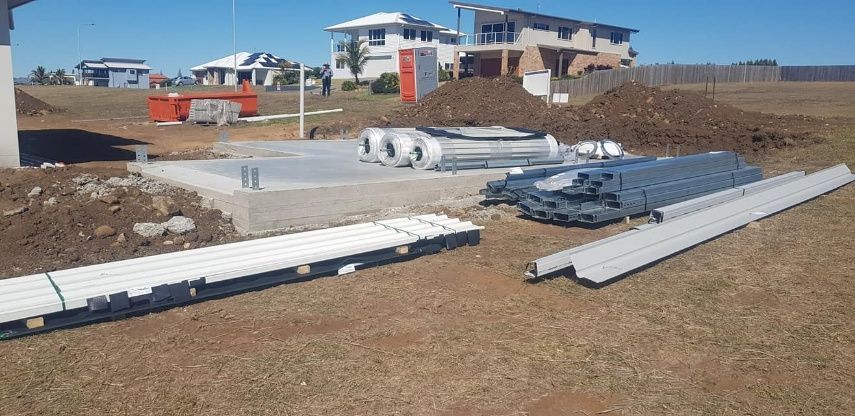 A Pile Of Pipes Is Sitting On The Ground In Front Of A House Under Construction — Bushman Sheds in Bundaberg East, QLD