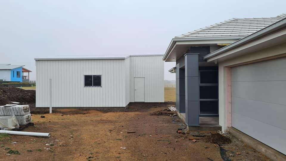 A White Shed Is Being Built Next To A House — Bushman Sheds in Bargara, QLD