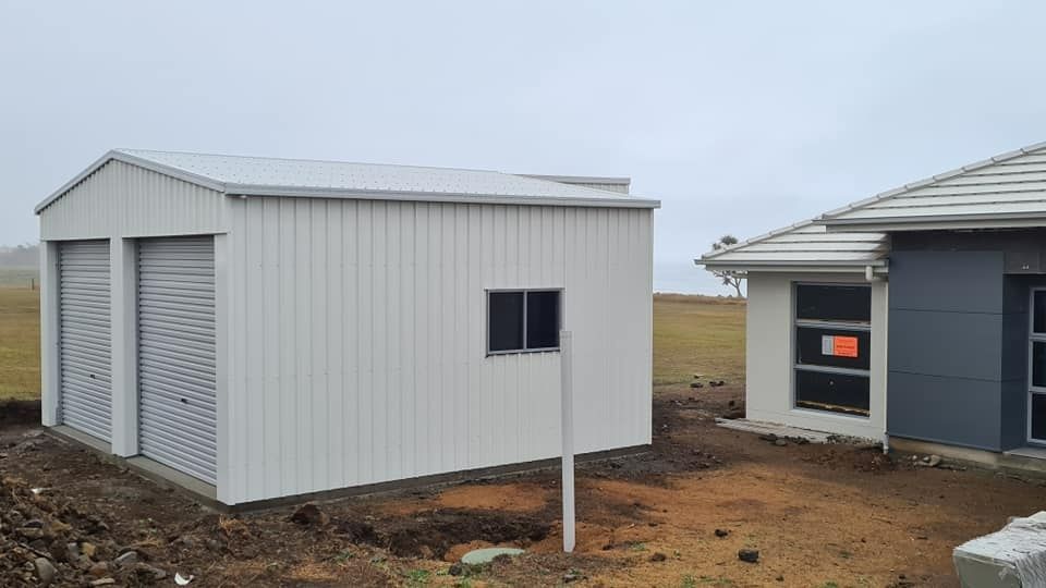 A White Garage Is Sitting Next To A House Under Construction — Bushman Sheds in South Kolan, QLD