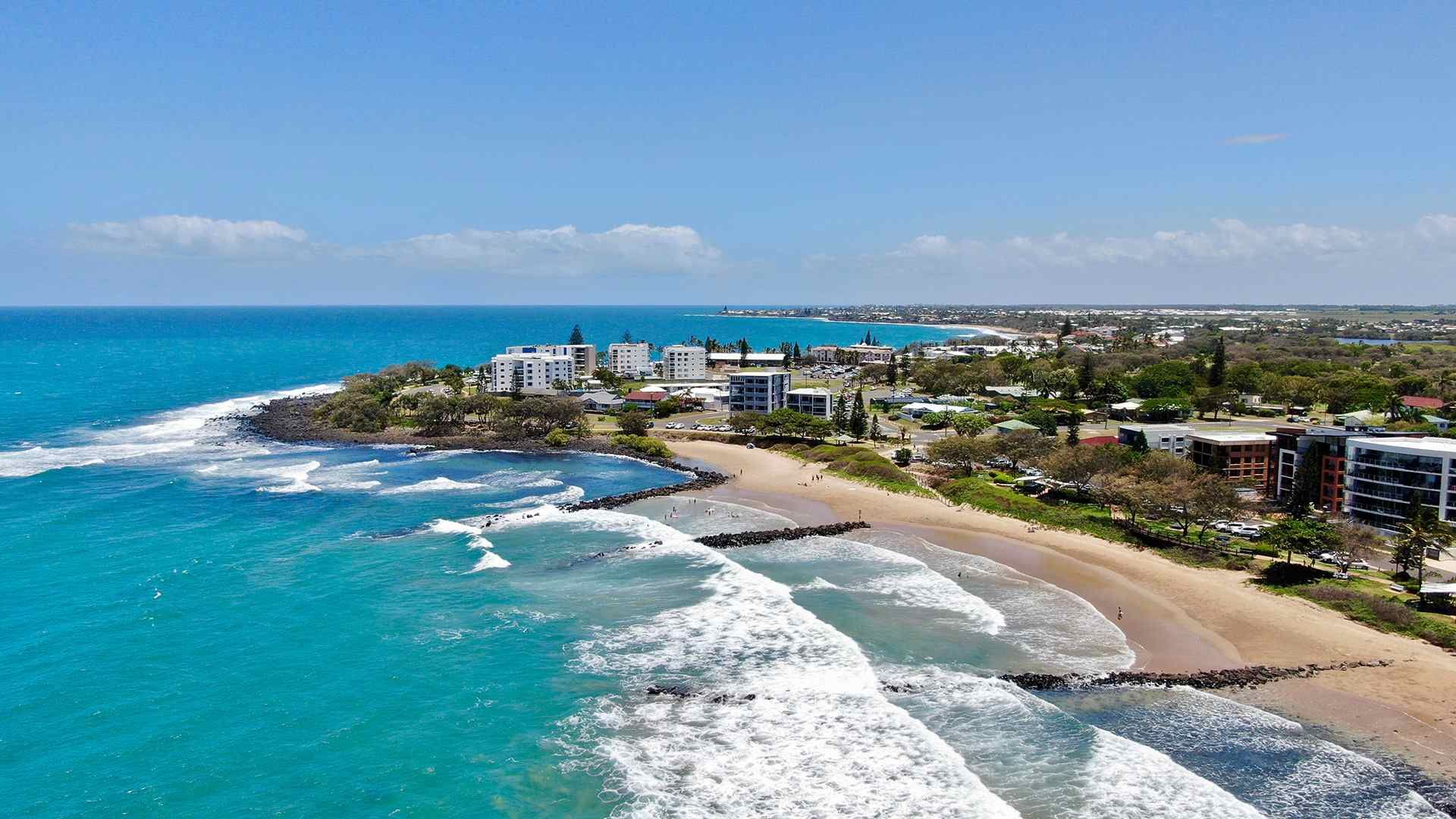 An Aerial View Of A Beach With Waves Crashing On The Shore — Bushman Sheds in Bargara, QLD