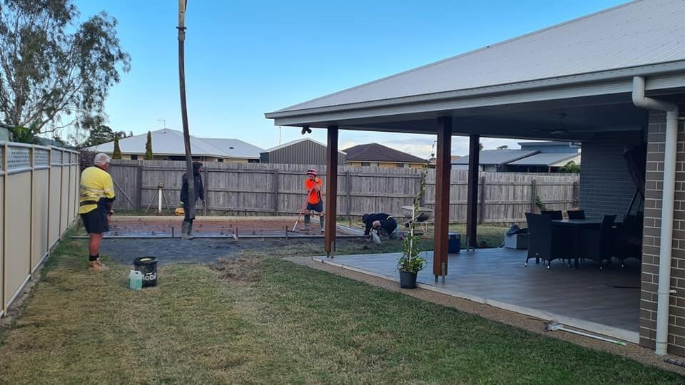 A Group Of People Are Working In A Backyard Next To A House — Bushman Sheds in Bundaberg, QLD