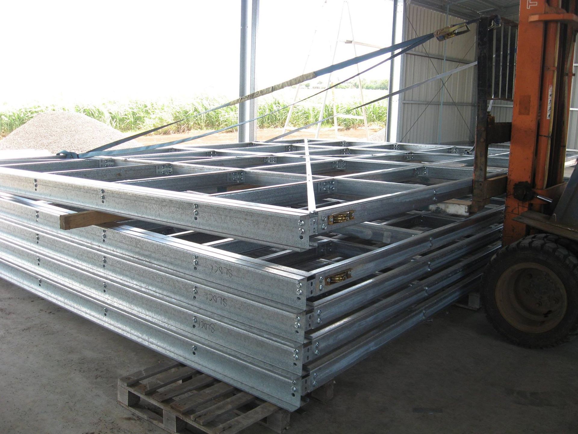 A Forklift Is Carrying A Stack Of Metal Frames — Bushman Sheds in Bundaberg East, QLD