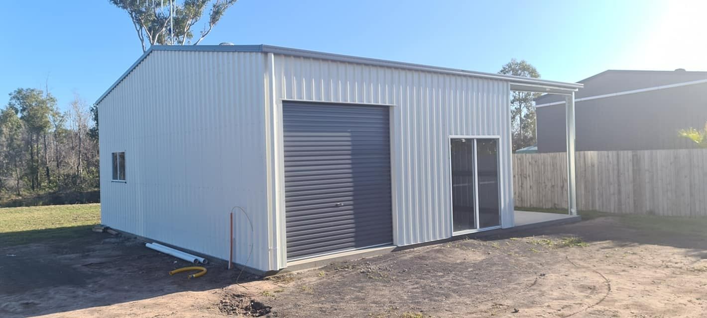 A White Garage With A Black Door Is Sitting In The Middle Of A Dirt Field — Bushman Sheds in Bundaberg East, QLD
