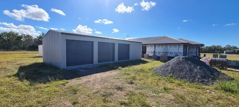 A Shed Is Sitting In The Middle Of A Grassy Field Next To A House — Bushman Sheds in Bundaberg East, QLD