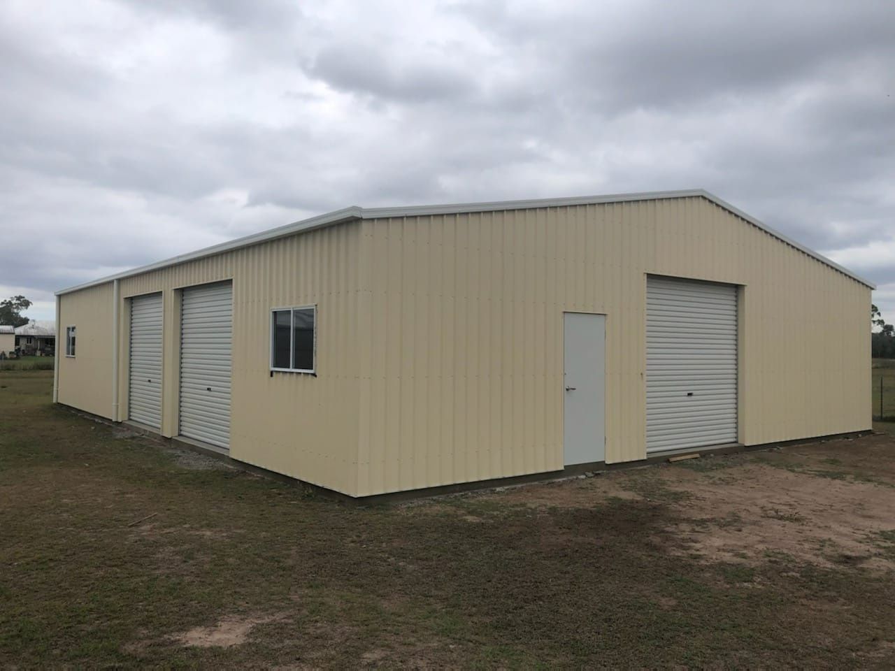 A Large Metal Building With White Doors And Windows Is Installed In The Middle Of A Grassy Field — Bushman Sheds in Bundaberg East, QLD