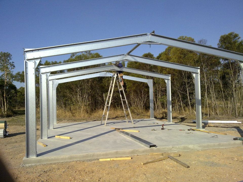 A Man Is Standing On A Ladder In Front Of A Metal Structure — Bushman Sheds in Bundaberg East, QLD