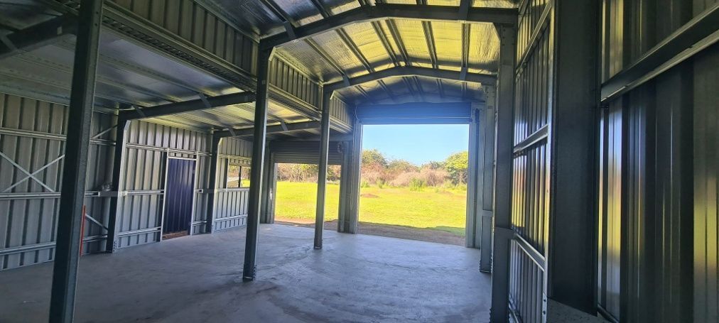 A Large Empty Building With A Large Garage Door Open — Bushman Sheds in Bundaberg East, QLD