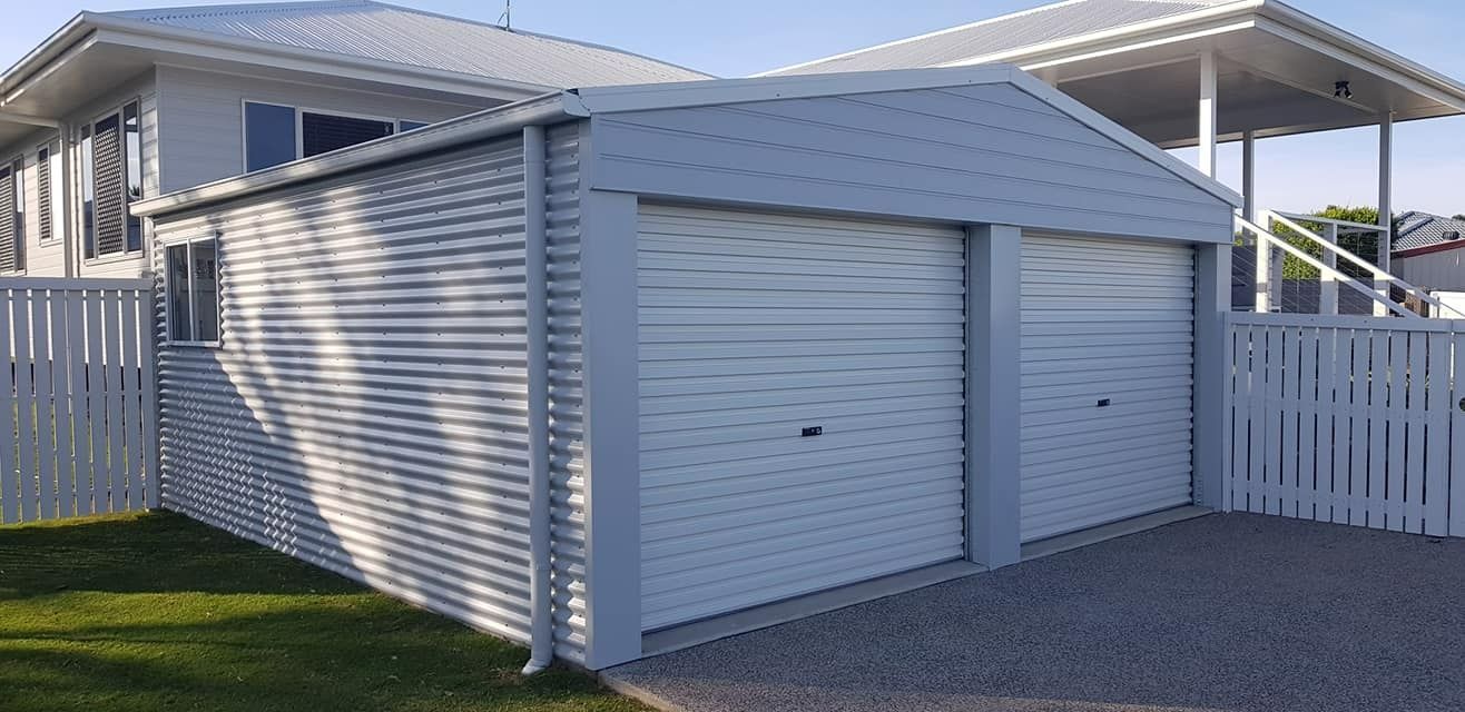 A White Garage With A White Fence In Front Of A House — Bushman Sheds in Bundaberg East, QLD