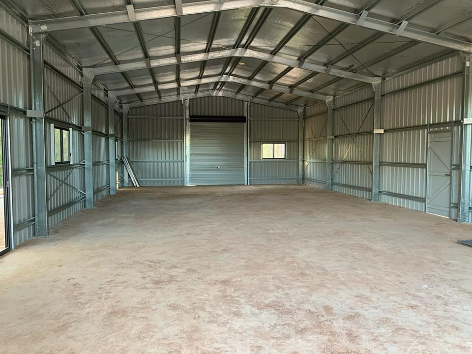 A Large Empty Warehouse With A Sliding Door And A Ladder — Bushman Sheds in Bundaberg East, QLD
